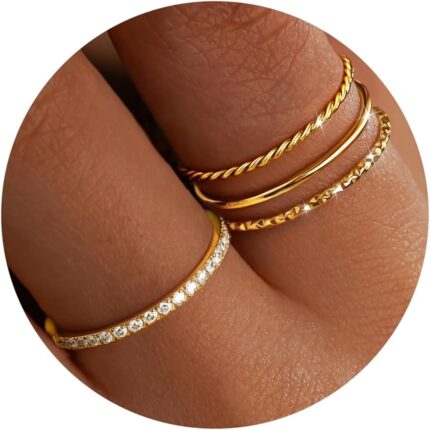 Close-up of four dainty 14K gold plated stacking rings with clear created diamonds, styled on a woman's fingers.