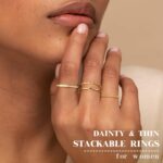 Close-up of four dainty 14K gold plated stacking rings with clear created diamonds, styled on a woman's fingers.