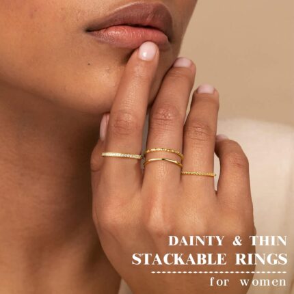 Close-up of four dainty 14K gold plated stacking rings with clear created diamonds, styled on a woman's fingers.