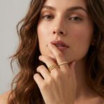 Close-up of four dainty 14K gold plated stacking rings with clear created diamonds, styled on a woman's fingers.