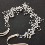 Close-up of a silver bridal headpiece featuring delicate metal leaves, luminous pearls, and sparkling clear rhinestones.